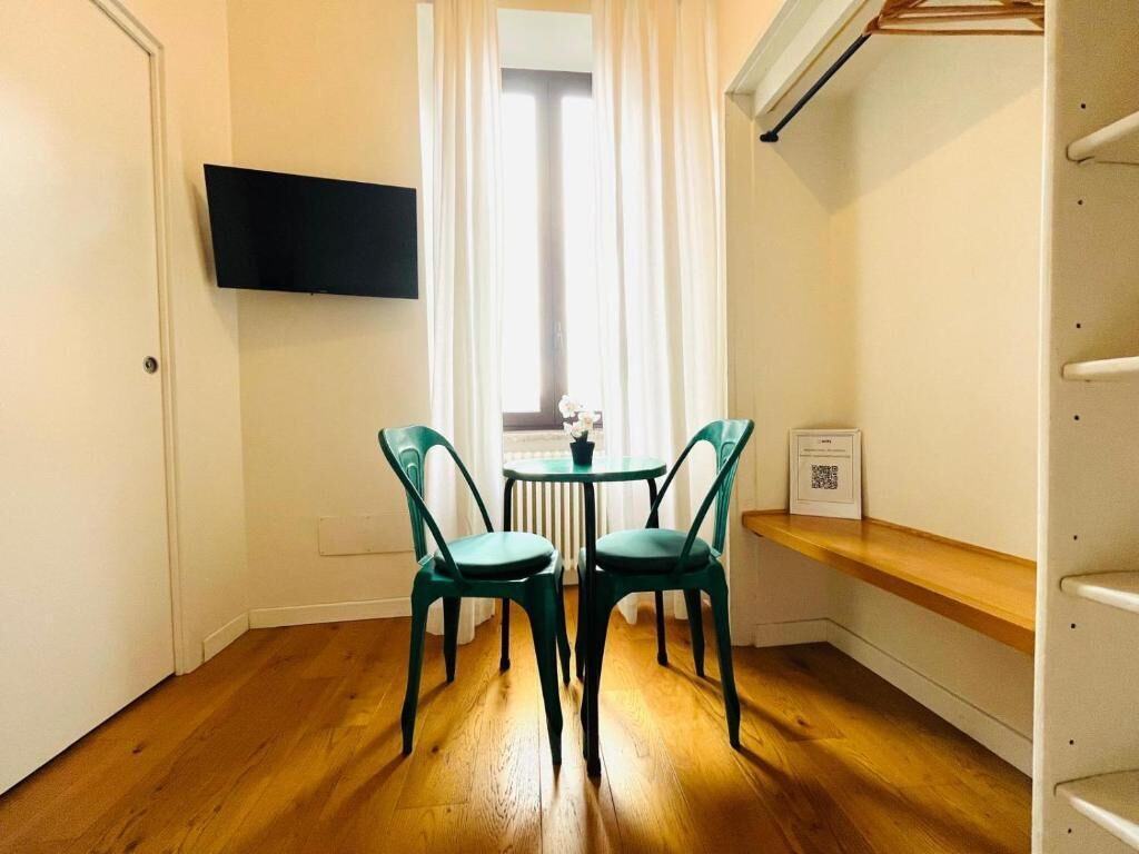 A room with a wooden floor, a small table with two chairs, a mounted TV, and a window with curtains.