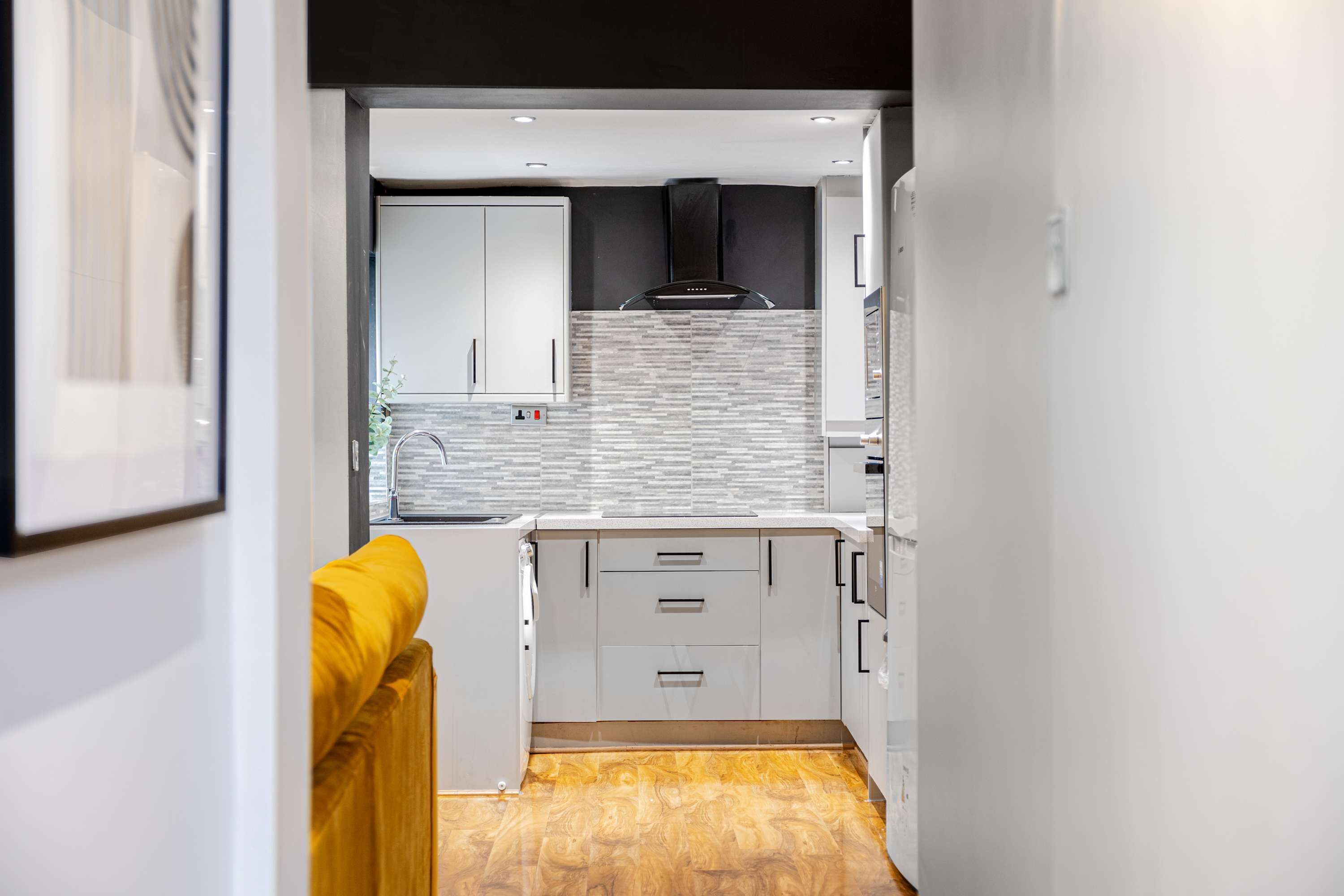 A modern kitchen with white cabinets, a black range hood, and a patterned backsplash.