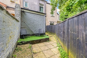 A backyard with a brick wall, a wooden fence, a paved patio, and a chair. - 3 BR Home 3 min Close to MCR City Centre Free Park (Manchester)