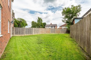 A residential backyard with a wooden fence, a well-maintained lawn, and a brick house.