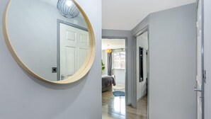 A hallway with a round mirror, a door, and a glimpse of a bedroom with a bed and curtains. - Trafford Centre Cityscape Hideaway Free Parking (Manchester)