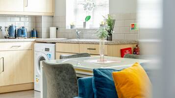 Et moderne køkken med vaskemaskine, et spisebord med stole og et vindue med planter.