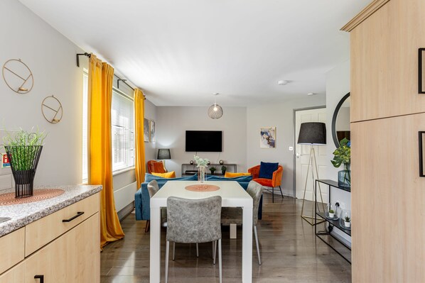 A modern kitchen with a dining area, wooden cabinets, a TV, and a plant on the counter.