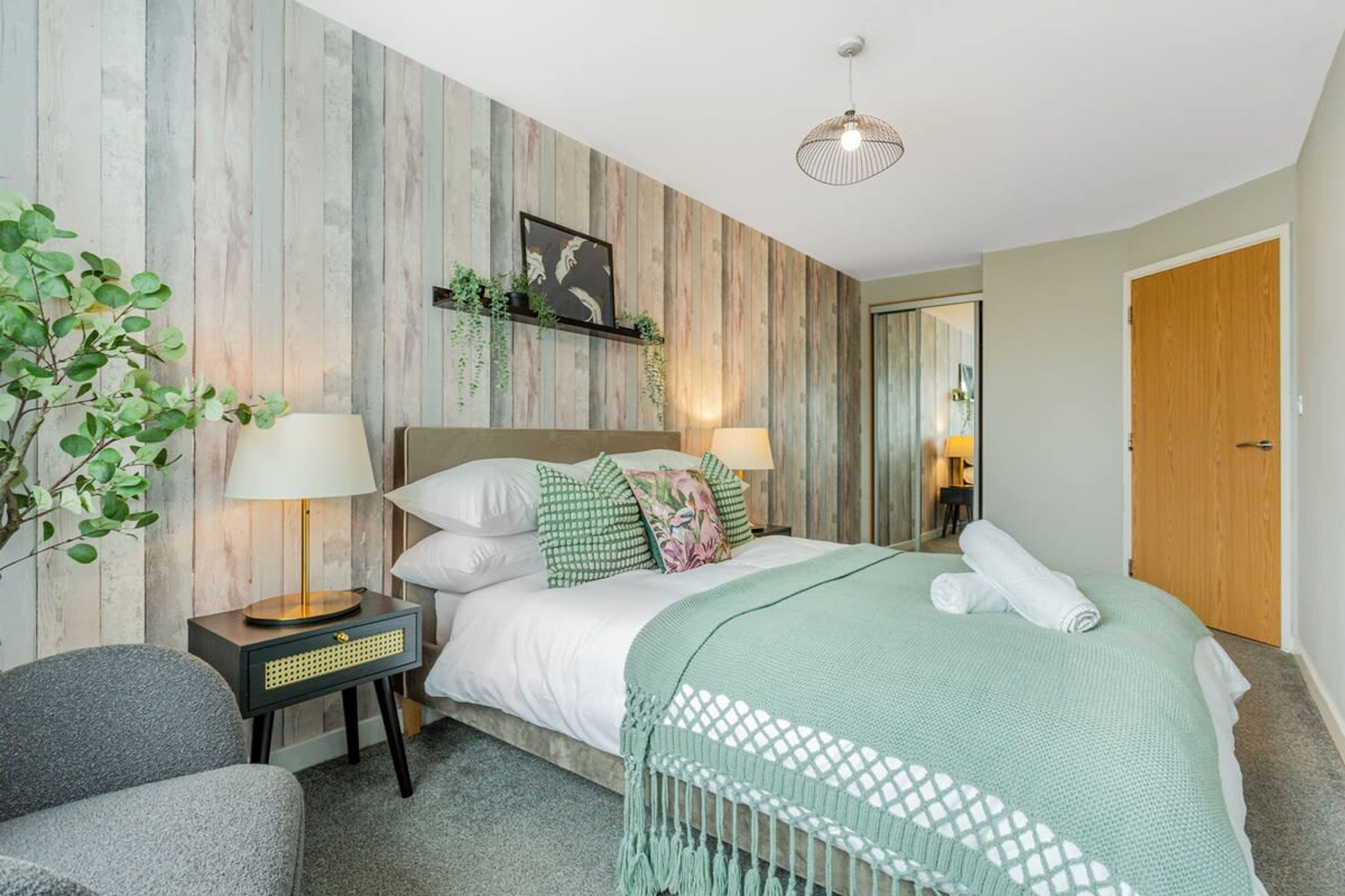 Ein Schlafzimmer mit einem Bett, Nachttischlampen, einer Pflanze und einer Holzwand.
