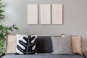 A sofa with three cushions, a wall with three artworks, and a potted plant. - Urban Chic 2-br Flat Trafford Centre Free Parking (Manchester)