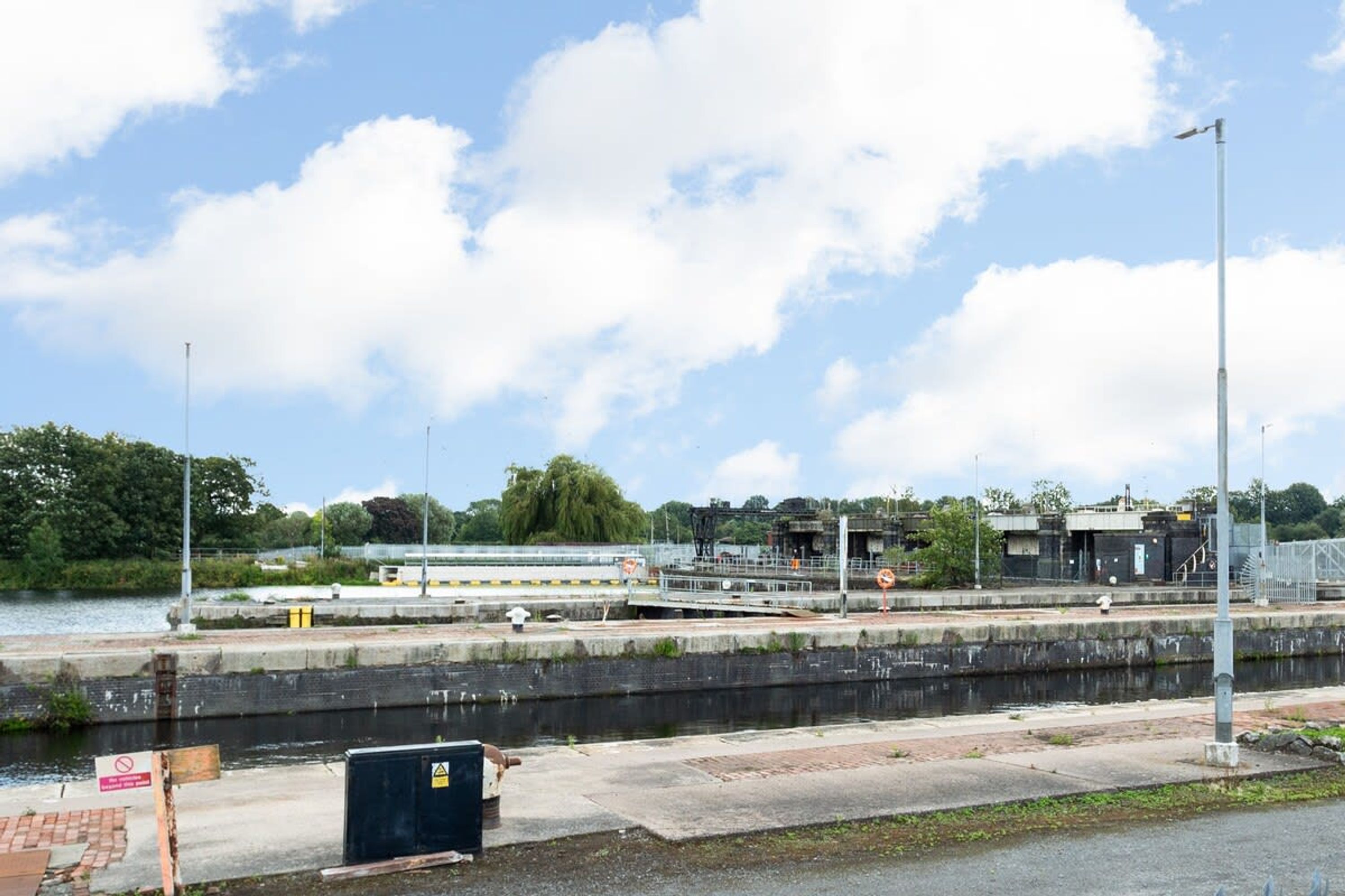 Ein Fluss mit Schleusen, einer Brücke und Industriegebäuden im Hintergrund.