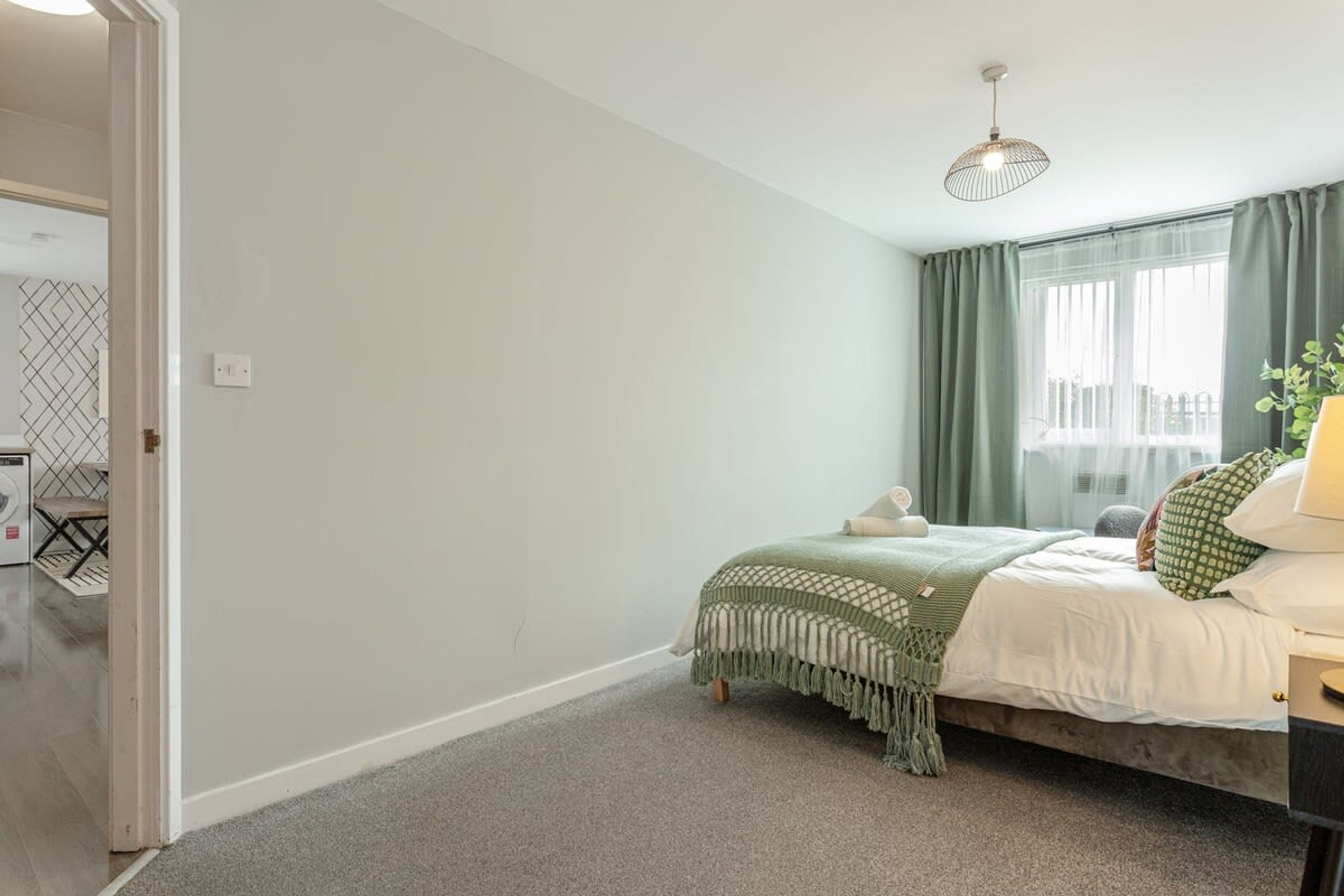A bedroom with a bed, a nightstand, a lamp, and a window with curtains.