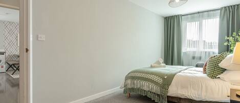 A bedroom with a bed, a nightstand, a lamp, and a window with curtains.