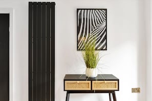 A room with a black and white striped wall panel, a framed abstract art piece, and a small table with a potted plant. - Salford Quays Luxury Safari Retreat Free Parking (Salford)
