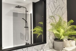 Un bagno moderno con box doccia in vetro, rubinetto nero e una felce in vaso.