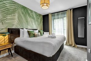 A modern hotel room with a large bed, a nightstand with a lamp, a wall-mounted TV, and a large window with curtains. - Salford Quays Luxury Safari Retreat Free Parking (Salford)