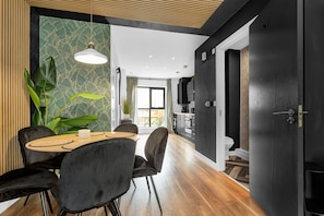 A modern kitchen with dark cabinetry, a dining area with a round table and chairs, and a large potted plant. - Salford Quays Luxury Safari Retreat Free Parking (Salford)