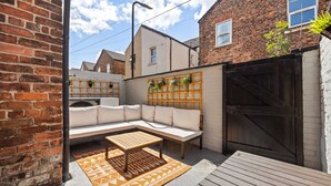 A brick house with a white exterior, a black gate, a wooden bench, and a white sofa. - Sleeps 14 The Old Trafford Zen by Genesis Living (Manchester)