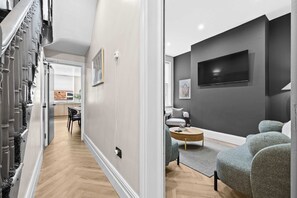 Una sala de estar moderna con televisor de pantalla plana, sofá gris y una zona de comedor con mesa y sillas.