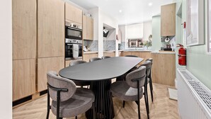 A modern kitchen with wooden cabinets, a central island, and a dining area with grey chairs. - Sleeps 14 The Old Trafford Zen by Genesis Living (Manchester)