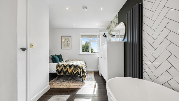A modern bedroom with a bed, a window, a radiator, and a bathroom with a white bathtub. - 2 Free Park Space The Quays- Sleeps 8 2 Ensuites (Salford)