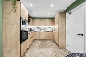 A kitchen with wooden cabinets, a microwave, and a herringbone-patterned floor. - Amazonian Luxury Family Home MCR City Centre Park (Manchester)