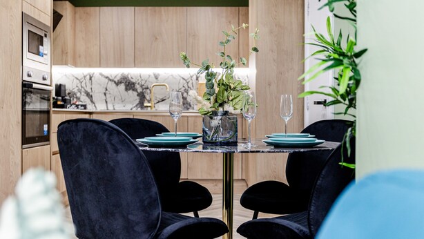 Un comedor moderno con salpicadero de mármol, armarios de madera y un jarrón central con follaje.