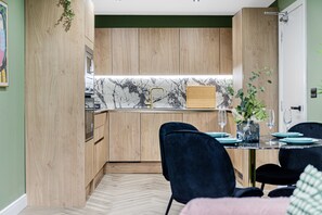 A modern kitchen with wooden cabinets, a marble backsplash, and a dining area with a glass table and dark chairs. - Amazonian Luxury Family Home MCR City Centre Park (Manchester)