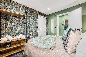A bedroom with a bed, a wooden shelf with towels, a mirror, and a door. - Amazonian Luxury Family Home MCR City Centre Park (Manchester)