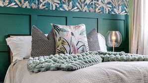 Una cama bien hecha con un cojín estampado, un cabecero verde y una lámpara de noche.