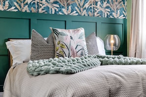 A neatly made bed with a patterned pillow, a green headboard, and a bedside lamp. - Amazonian Luxury Family Home MCR City Centre Park (Manchester)