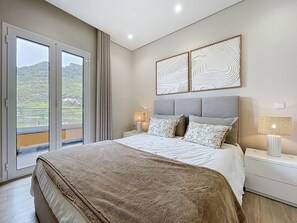 A bedroom with a bed, two bedside lamps, a nightstand, a sliding glass door to a balcony, and two wall art pieces. - Recanto do Sol by Atlantic Holiday (Machico)