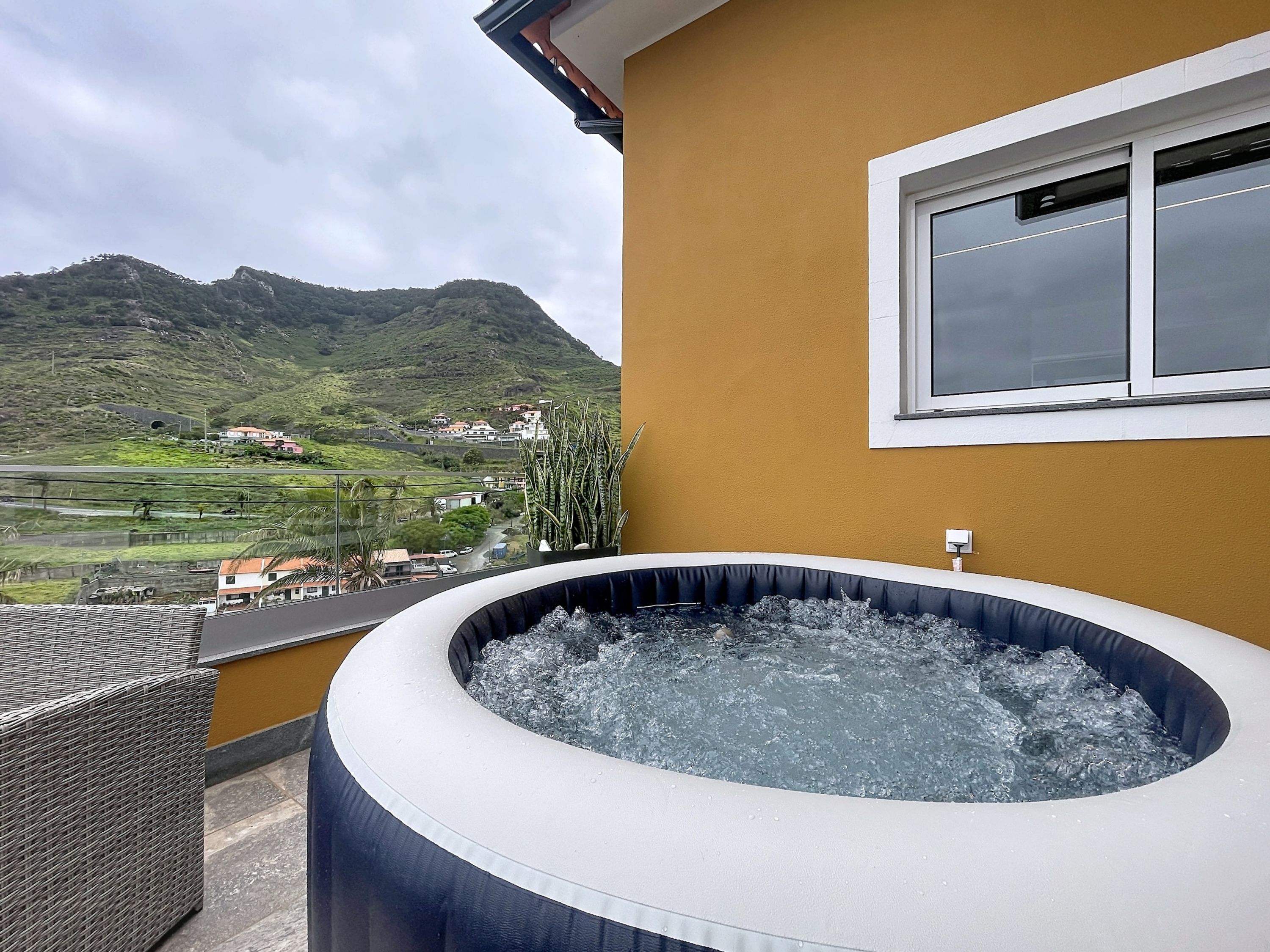 A hot tub with a mountain view, a window, and a wicker chair.