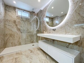 A modern bathroom with a marble wall, a large mirror, a shower, and a white vanity. - Recanto do Sol by Atlantic Holiday (Machico)