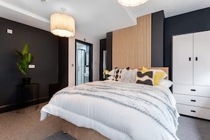 Un dormitorio moderno con una cama grande, una mesita de noche, una planta en maceta, un armario y una puerta que da a otra habitación.