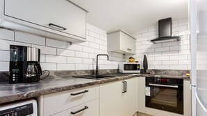 A modern kitchen with white cabinets, a built-in oven, a microwave, and a coffee maker.