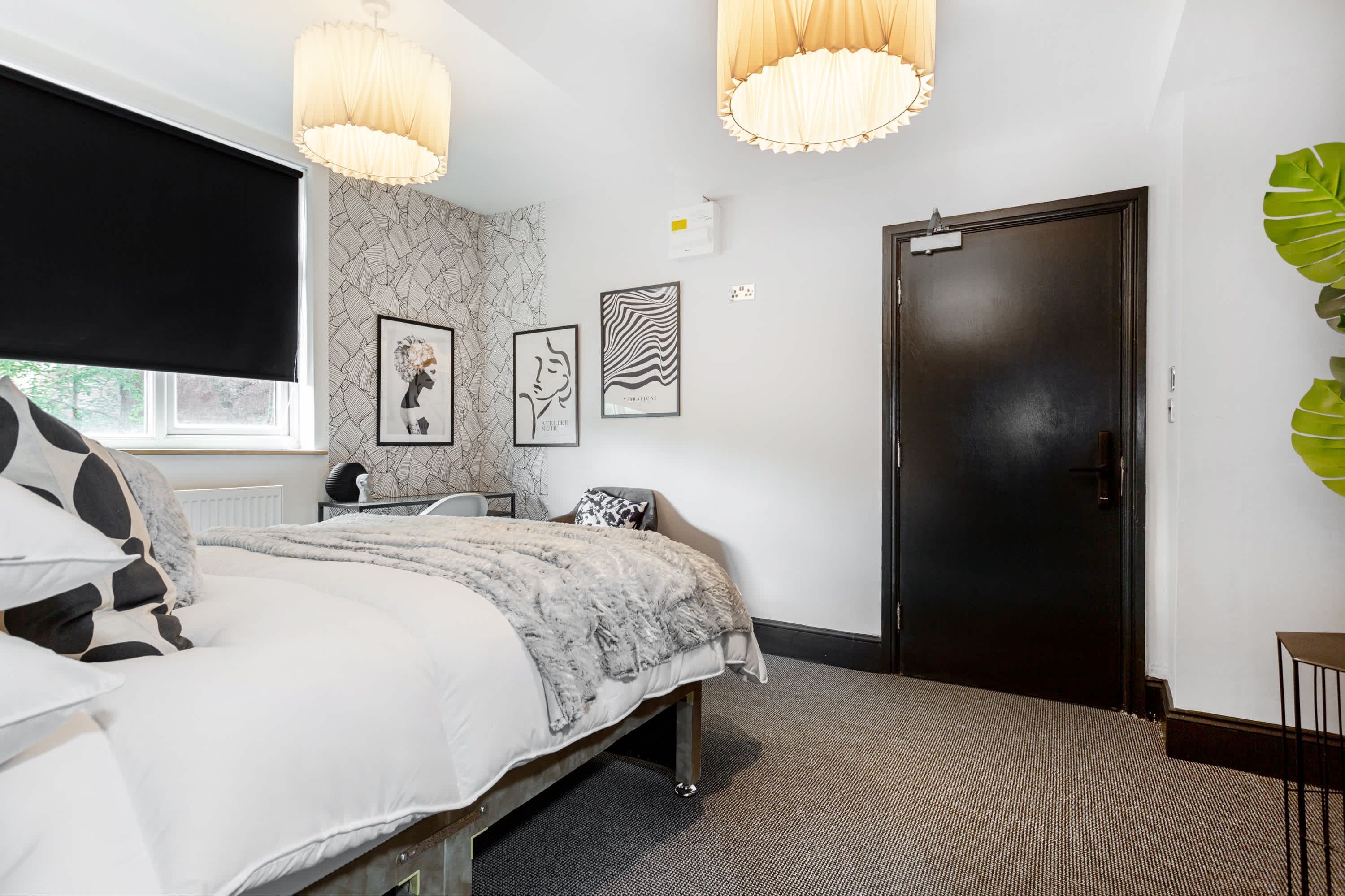 Une chambre à coucher avec un lit, une fenêtre munie d’un store noir, une porte et des œuvres d’art murales.