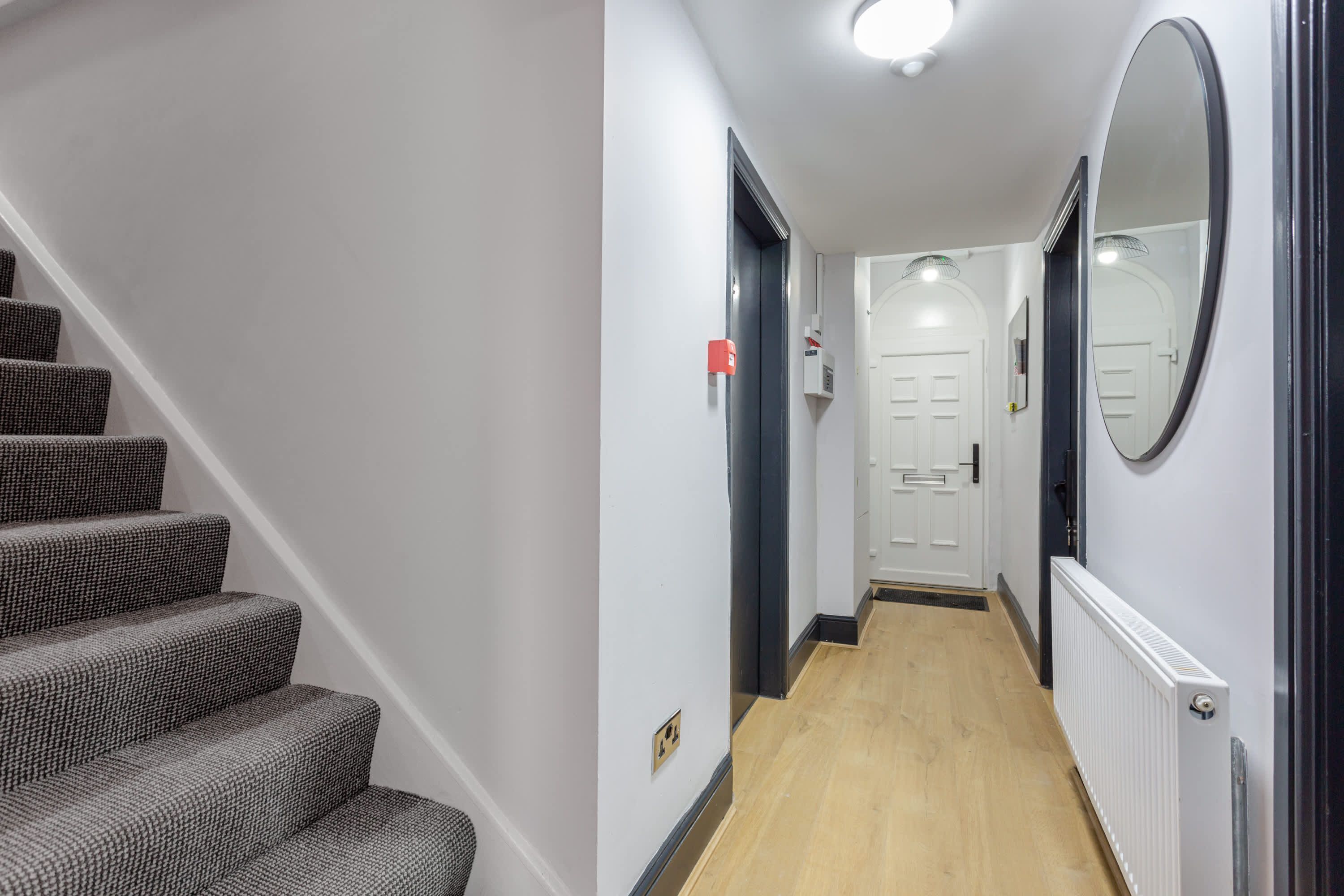 A hallway with a staircase, a door, a radiator, and a mirror.