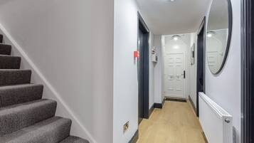 A hallway with a staircase, a door, a radiator, and a mirror.