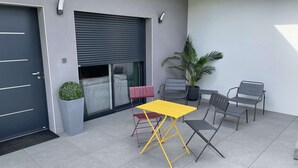 A modern outdoor patio with a yellow table and chairs, a potted plant, and a sliding door.