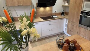 A modern kitchen with white cabinetry, a black range hood, and a tray of mugs.