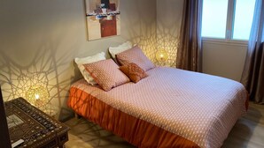 A bedroom with a large bed, a bedside table, a lamp, and a window with curtains.