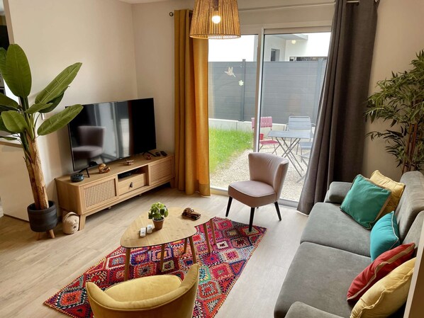 Uma sala de estar moderna com uma televisão de tela plana, um sofá, uma poltrona, uma mesa de centro e uma grande planta em vaso.