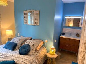 Quarto com cama, luminária de cabeceira, espelho fixado na parede e um pequeno banquinho com abajur.