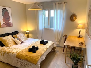 A bedroom with a bed, bedside lamps, a window with curtains, a small table with a lamp, and a wall decoration. - Havana - Air-conditioned 4* apartment with terrace and private garden (DRUMETTAZ CLARAFOND)
