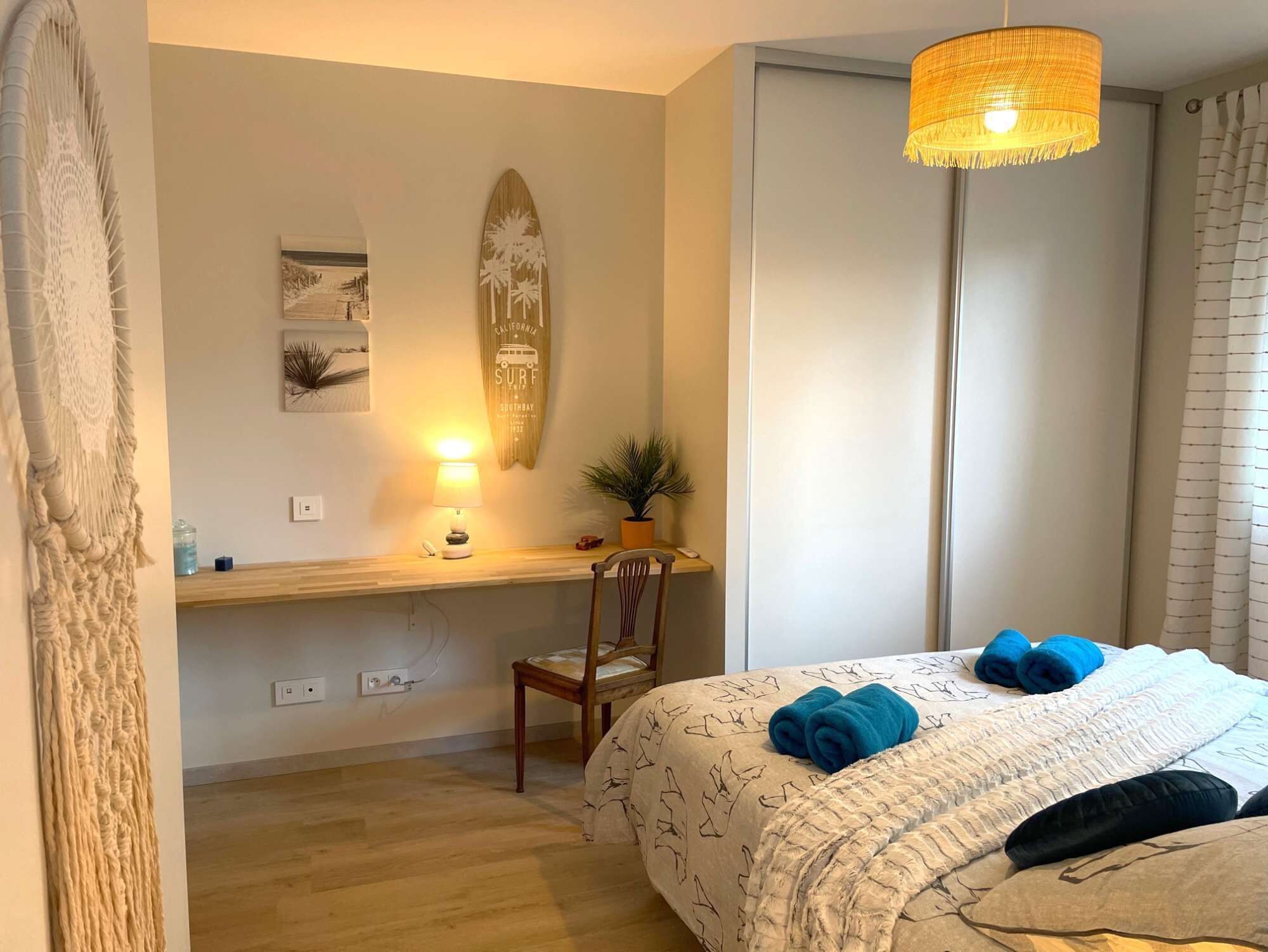 Ett sovrum med en säng, ett skrivbord, en stol, en lampa och en surfbräda som dekoration.