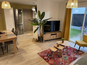 A modern living room with a TV, dining table, chairs, a coffee table, a large plant, and a colorful rug. - Havana - Air-conditioned 4* apartment with terrace and private garden (DRUMETTAZ CLARAFOND)