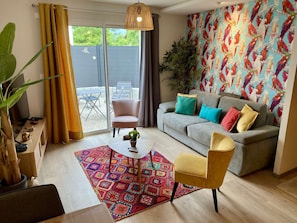 A living room with a grey sofa, colorful cushions, a patterned rug, and a large window with curtains. - Havana - Air-conditioned 4* apartment with terrace and private garden (DRUMETTAZ CLARAFOND)
