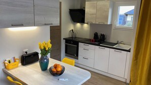 Una cucina moderna con zona pranzo, che include un tavolo in legno, sedie gialle, un vaso con fiori e una ciotola di frutta.