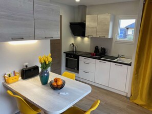 A modern kitchen with a dining area, featuring a wooden table, yellow chairs, a vase with flowers, and a bowl of fruit. - Yellow Cab - Air-conditioned 3* apartment with terrace and mountain views (DRUMETTAZ CLARAFOND)
