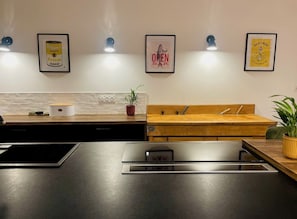 Una cocina moderna con encimera negra, armarios de madera, un fregadero y una estufa. Hay cuadros en la pared, incluyendo uno que dice 'OPEN BAR'.