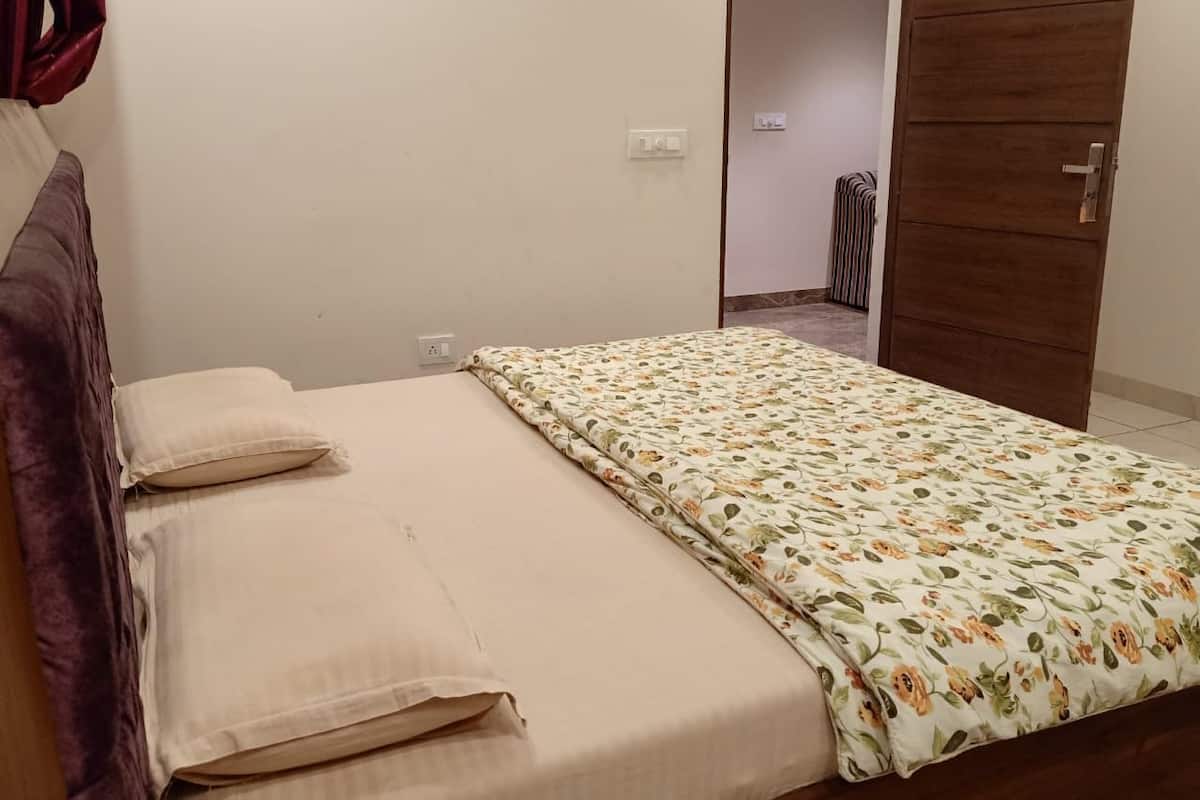Una cama individual con una colcha estampada floral y dos almohadas, una puerta de madera y un radiador al fondo.