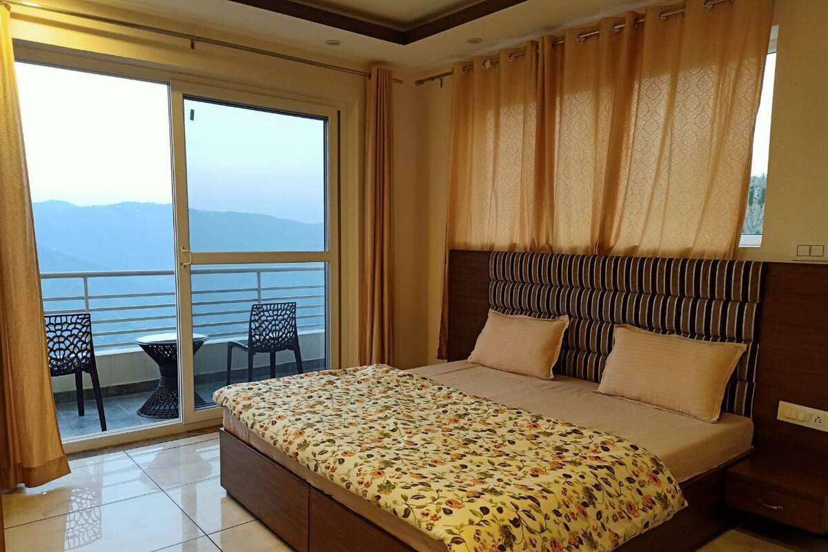 Un dormitorio con una cama grande, un balcón con sillas y vistas a las montañas.