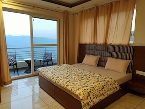 Un dormitorio con una cama grande, un balcón con sillas y vistas a las montañas.
