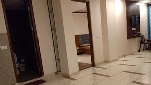 A hallway with a tiled floor, a wooden door, and a small seating area with a chair and table. - Pine Peak Kasauli (Kasauli)